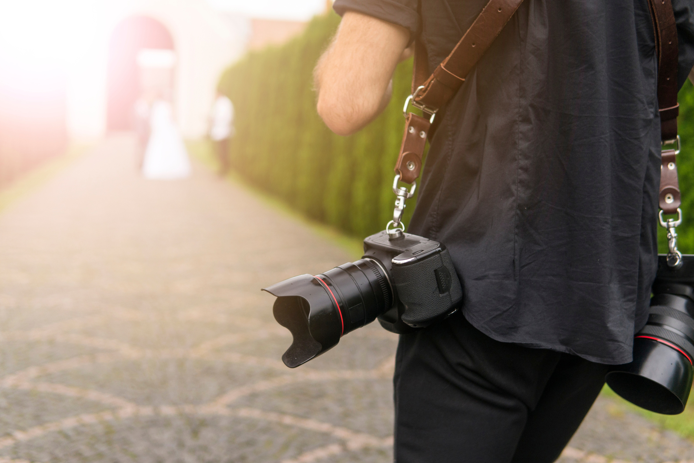 Professional wedding photographer takes pictures of the bride and groom in garden, the photographer in action with two cameras on a shoulder straps.